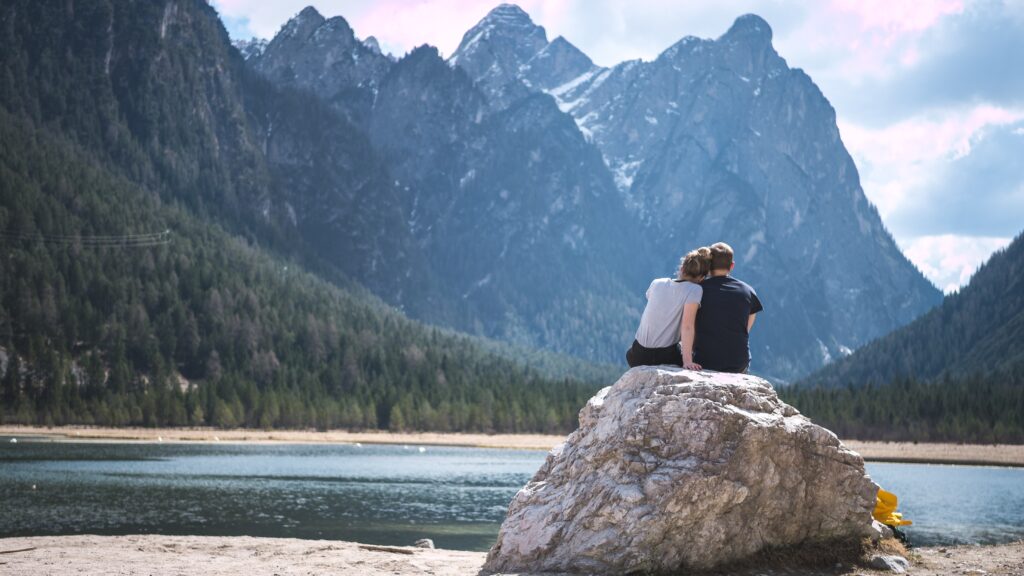 A couple sitting together on a rock by the mountains. They seem to be falling in love.